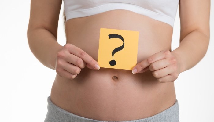 A woman holding a question mark over her slight baby bump.