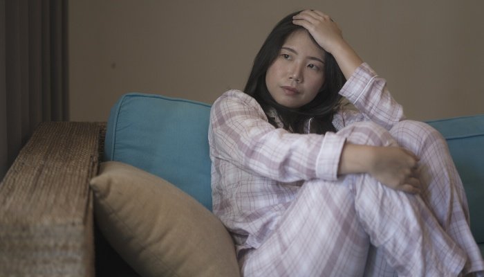 A sad woman in pajamas sitting on the couch in dimly lit room.