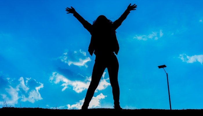 A woman with outstretched arms silhouetted against a sunrise.