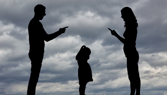 Two angry, fighting parents with a child in the middle silhoutted against a stormy sky.