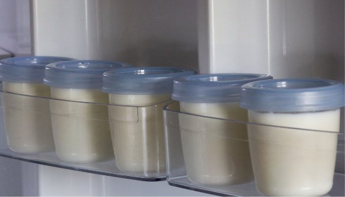 Small jars of stored breast milk in the compartment of a refrigerator door.
