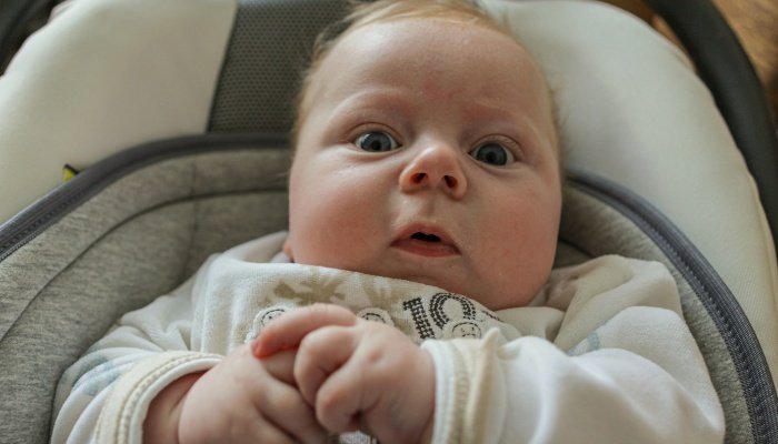 A baby looking very surprised lying in a reclining stroller.