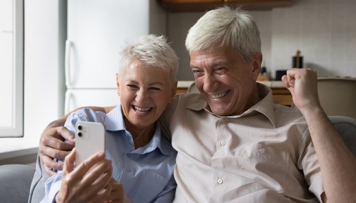 Grandparents looking at a phone with happy and surprised expressions on their faces.