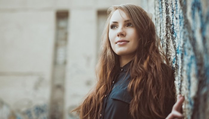 A woman leaning against a tree with a thoughtful expression on her face.
