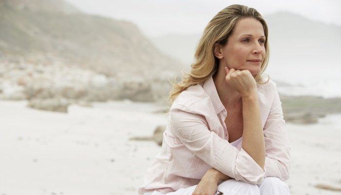 A woman sitting on a rock at the beach looking thoughtful and reflective.
