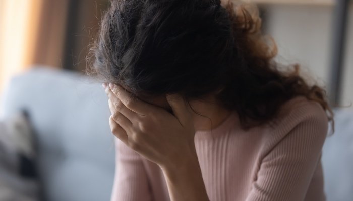 An upset woman sitting on a couch holding her head in her hand.