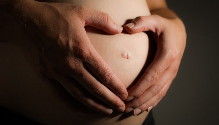 A woman making a heart with her hands over her pregnant belly.