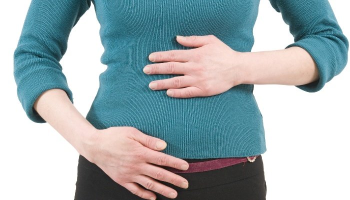 A woman in a blue sweater and jeans with both hands placed on her stomach.