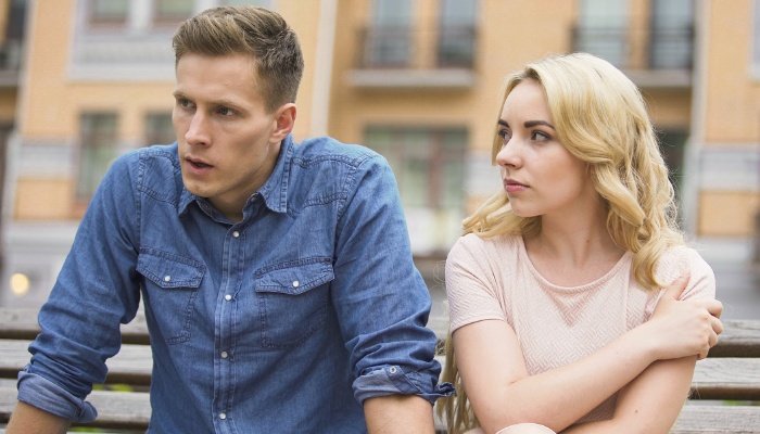 A woman and a jealous boyfriend sitting outside on a park bench.