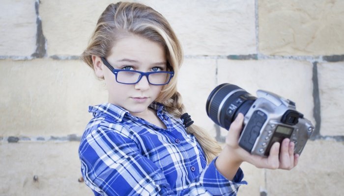 A young, arrogant girl in blue glasses and matching plaid shirt taking a photo of herself.