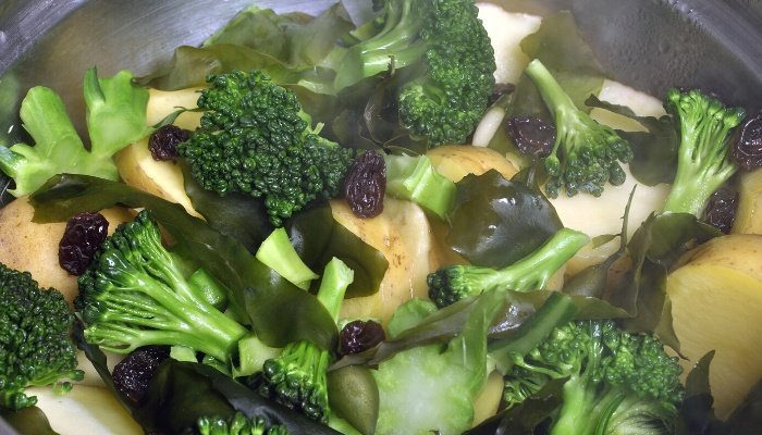 Assorted steamed veggies with raisins in a pan on the stove.