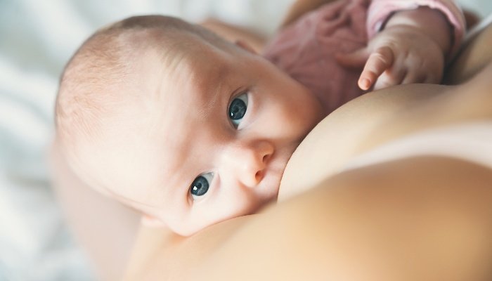 Looking over a breastfeeding mother's shoulder at her baby looking up at the camera.
