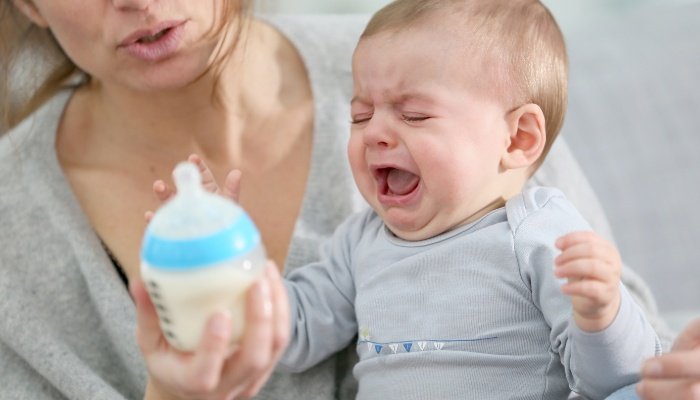 A baby crying and slapping away a bottle offered by her mother.