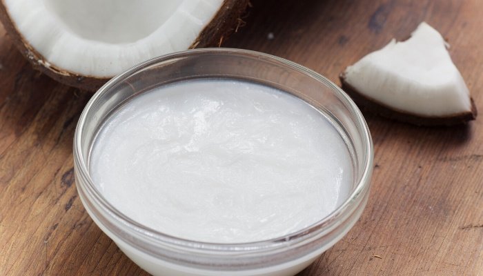 A small bowl of warmed coconut oil beside a freshly opened coconut.