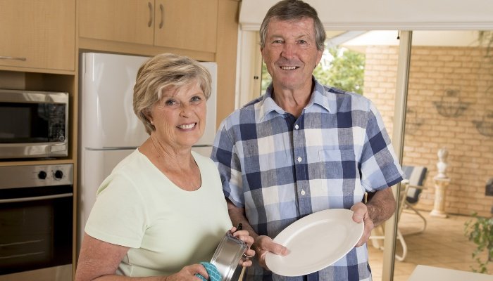 Grandparents happily washing dishes together.