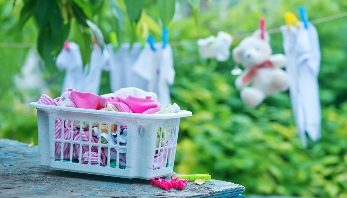 Clean baby clothes in a laundry basket and on a clothesline outside.