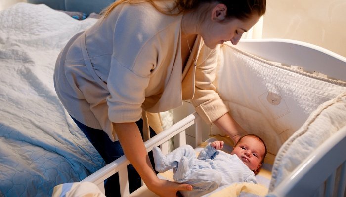 A young mother putting her awake baby in his crib to sleep.