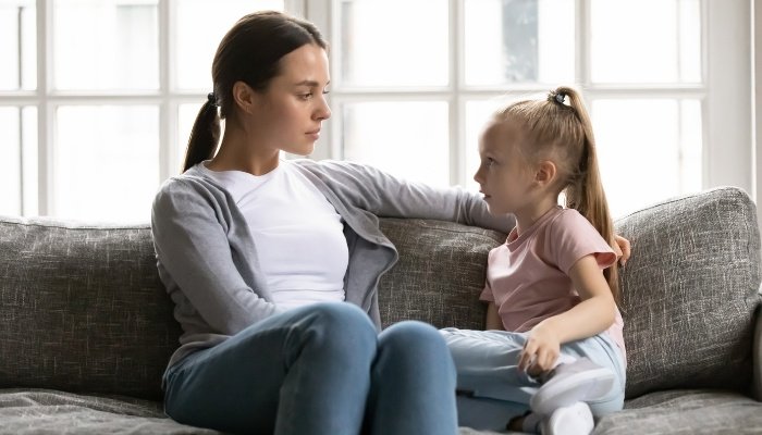 A woman and a young girl sit on the couch for a serious conversation.