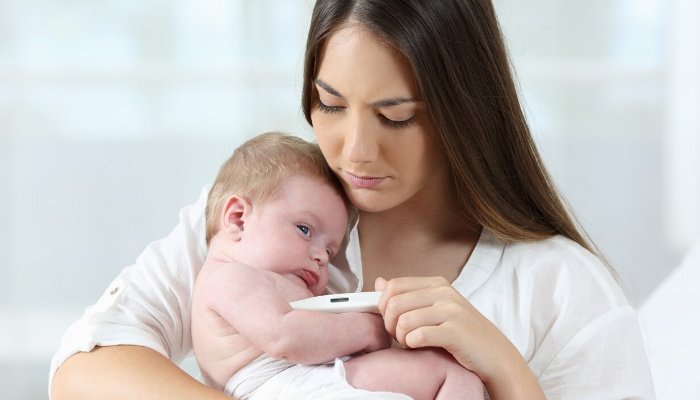A young mother checking her baby's temperature with a concerned look on her face.
