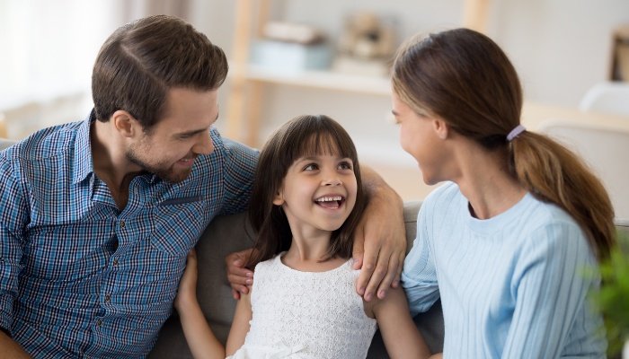 Happy parents sitting on the couch with their smiling daughter in the middle.