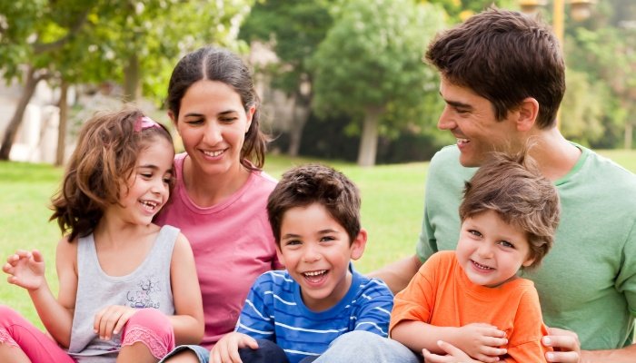 A happy couple and their three children sitting together in the middle of a park.