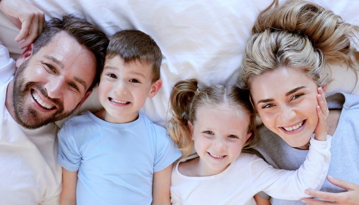 A young couple and their two children lounging in a big bed together.
