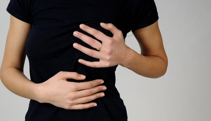 A woman in a black T-shirt holding her breast as if in pain.