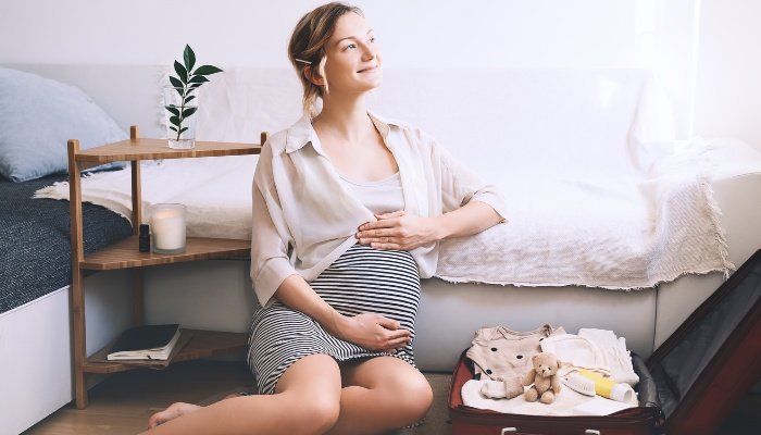 A pregnant woman sitting on the floor while packing her suitcase for the hospital.