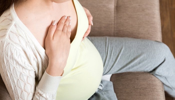 A pregnant lady holds her sore breast with one hand while rubbing it with the other.