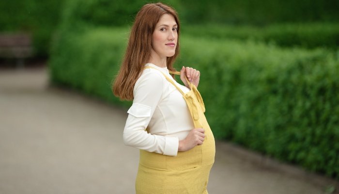 A pregnant woman in yellow overalls walking in a public garden.