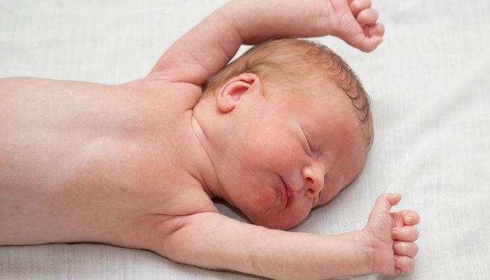 A red-headed baby asleep without a shirt and with his arms raised over his head.
