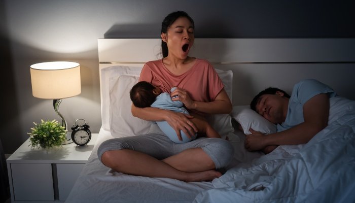 Sleepy parents awake in bed with their newborn during the night.