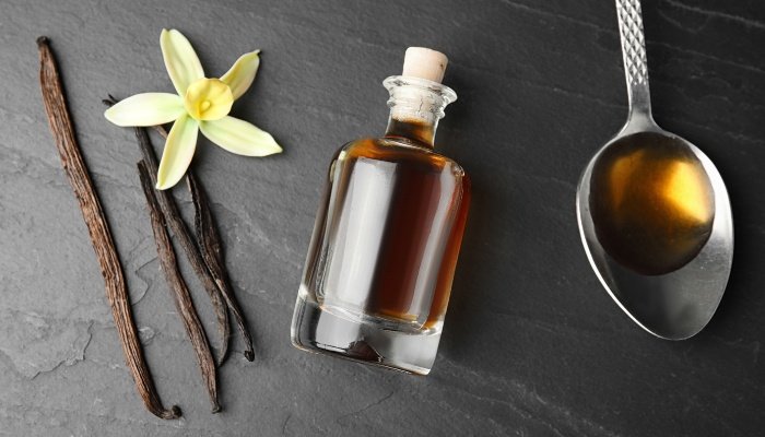 Vanilla beans, extract, and flowers arranged artfully on a table.