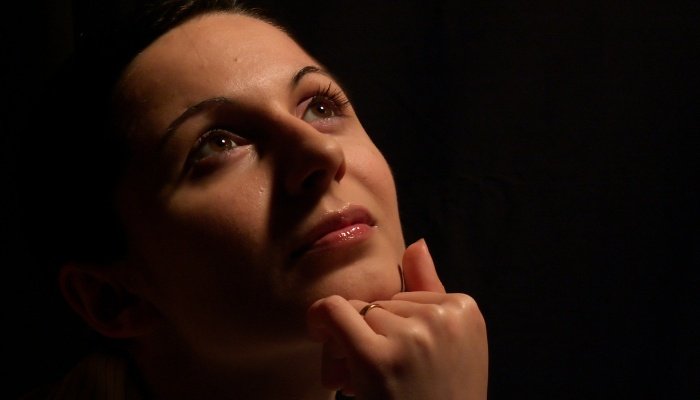 A young woman with her hand propped under her chin daydreams against a black background.