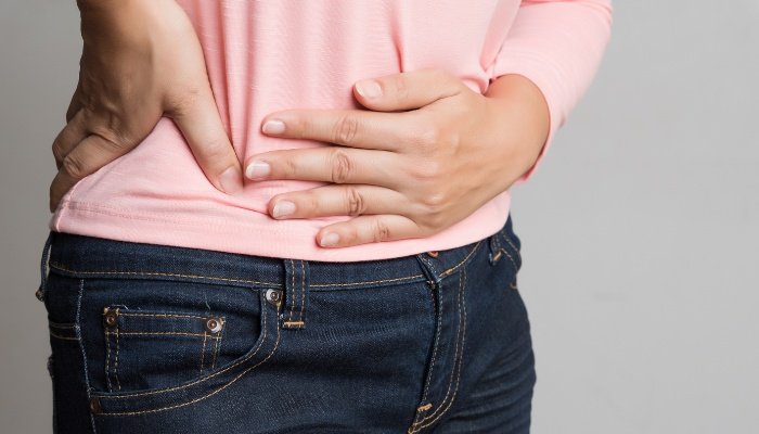 A woman wearing a pink top and jeans holding her stomach as if in pain.