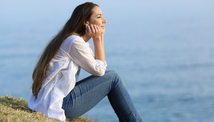 A young woman gazing at the ocean while daydreaming.