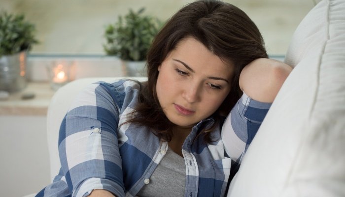 A woman is curled up on the couch mourning the loss of a pregnancy.