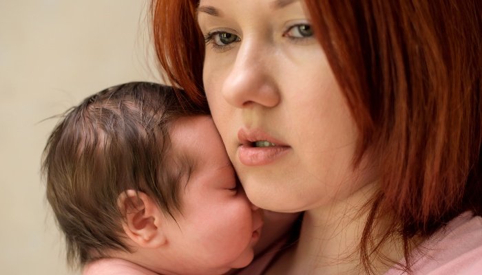 A worried mother with red hair holding her newborn upright against her body.