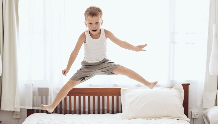A young boy jumping on the bed in front of a large window.