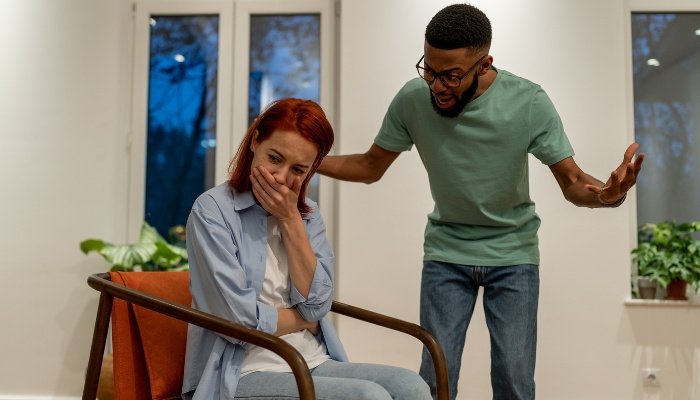A angry man shouting at a woman sitting in a chair.