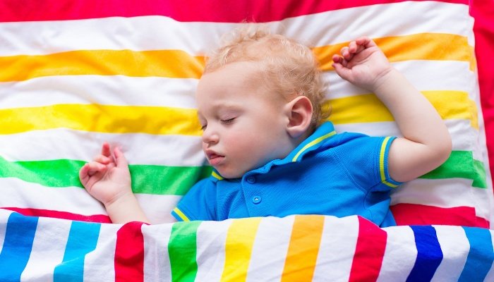 A little boy asleep under brightly striped toddler bedding.