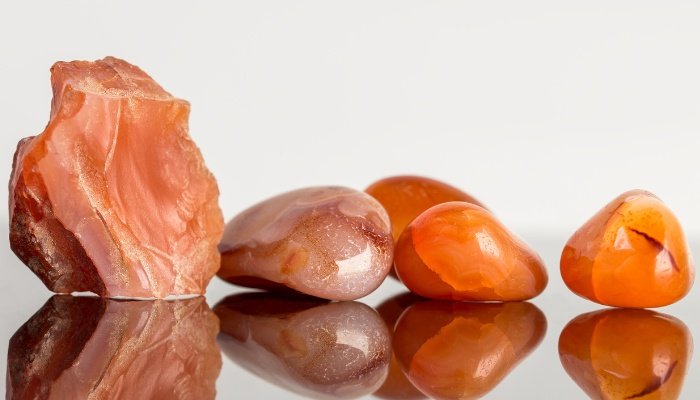 Rough and finished carnelian crystals on a mirrored surface.