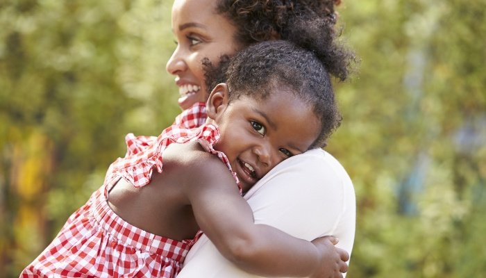 A young girl in a red-checked dress hugging her mother.