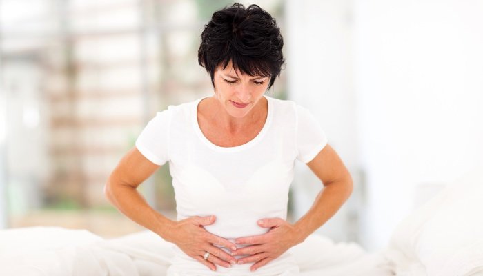 A woman feeling pain from constipation sitting on a bed dressed in white.