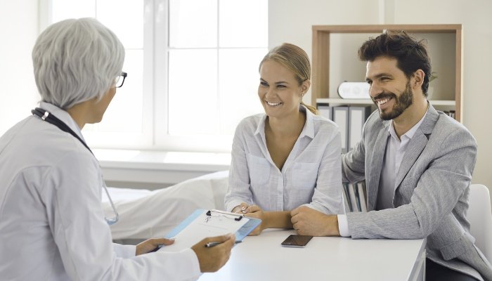 A young couple speaking with a fertility doctor and looking pleased.