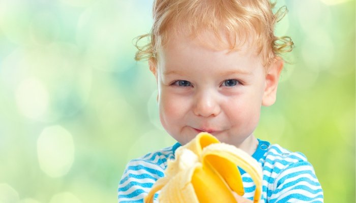 A cute toddler happily snacking on a banana while outside.