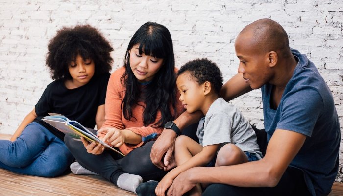 A blended family sitting on the floor reading a book together.