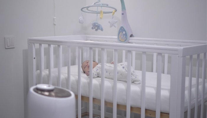 A humidifier in the nursery with a newborn lying in his crib in the background.