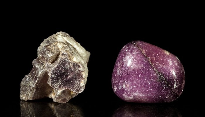 One rough and one finished lepidolite crystal on black.