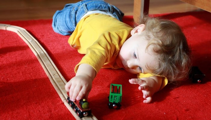 A little boy lying on the floor playing with a wooden train set.